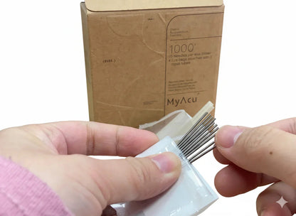 holding a small packet of needles with a cardboard box labeled 'MyAcu' in the background.